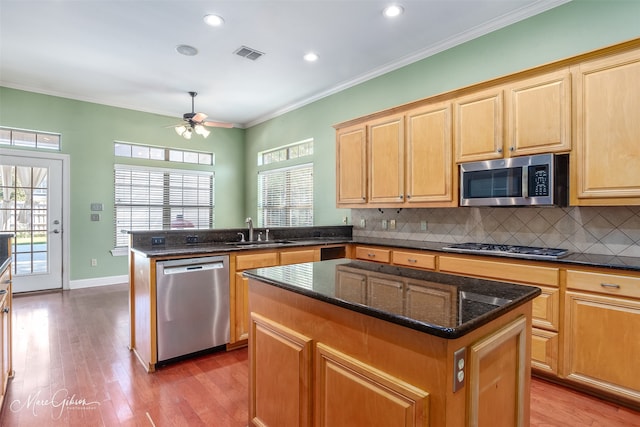 kitchen with sink, a kitchen island, stainless steel appliances, crown molding, and hardwood / wood-style floors