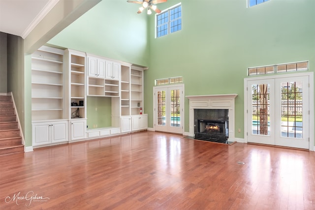 unfurnished living room with a towering ceiling, a fireplace, hardwood / wood-style flooring, and french doors