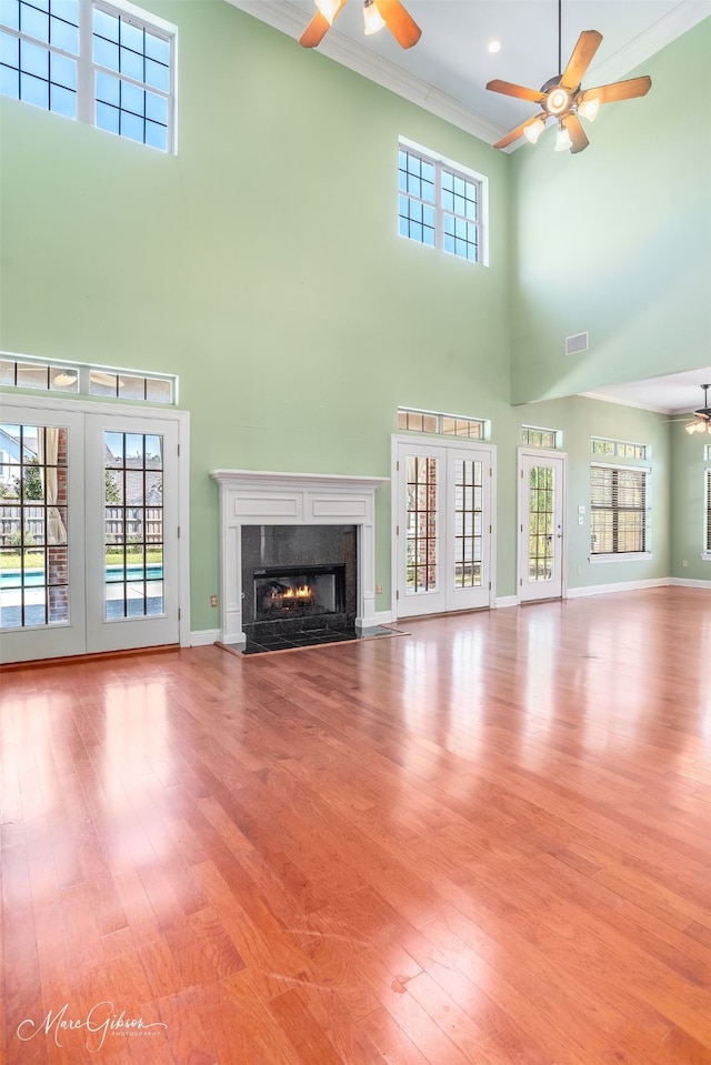 unfurnished living room with light hardwood / wood-style floors, a towering ceiling, crown molding, french doors, and a premium fireplace