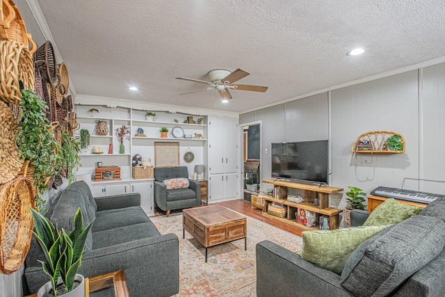 living room with light wood-type flooring, a textured ceiling, ceiling fan, and ornamental molding