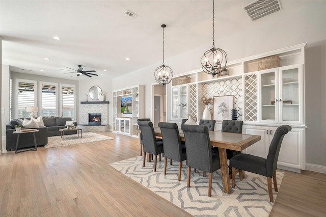 dining space with a fireplace, light hardwood / wood-style floors, and ceiling fan