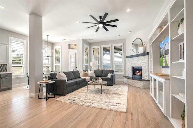 living room with light wood-type flooring, a stone fireplace, ceiling fan, and a healthy amount of sunlight