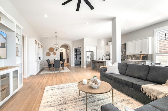 living room with ceiling fan with notable chandelier, light hardwood / wood-style floors, built in features, and sink