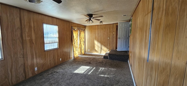 empty room featuring a textured ceiling, a ceiling fan, visible vents, carpet flooring, and wooden walls