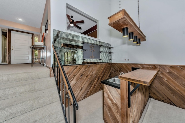 stairway featuring carpet, ceiling fan, and wooden walls