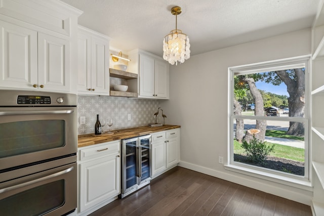 kitchen featuring white cabinetry, pendant lighting, stainless steel double oven, beverage cooler, and wood counters