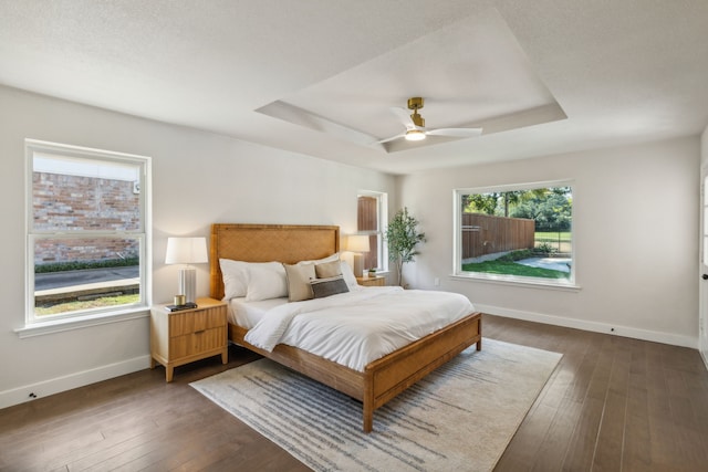 bedroom with ceiling fan, a textured ceiling, a tray ceiling, and dark hardwood / wood-style flooring