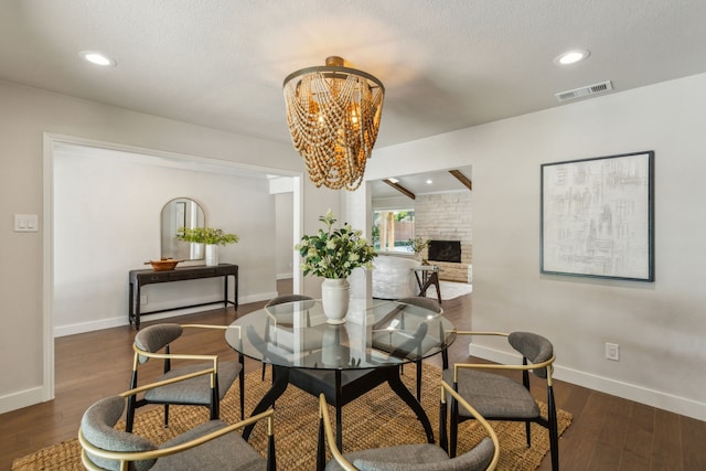 dining space featuring a textured ceiling, a fireplace, dark wood-type flooring, and a chandelier