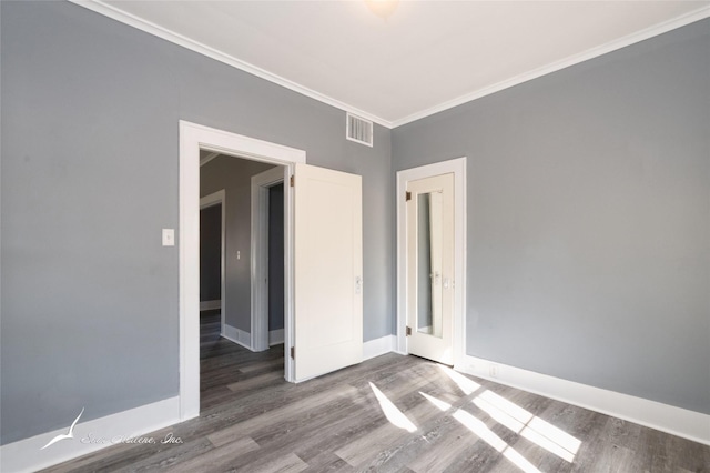 empty room featuring wood finished floors, crown molding, baseboards, and visible vents