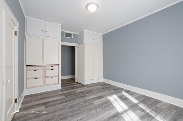 unfurnished bedroom featuring a closet, visible vents, baseboards, ornamental molding, and wood finished floors