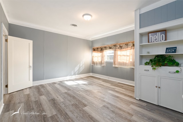 empty room with light wood-type flooring, crown molding, and built in shelves