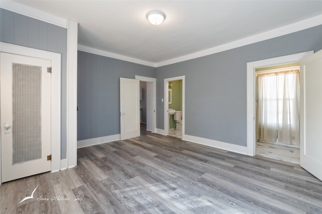 unfurnished bedroom with a closet, ensuite bath, hardwood / wood-style floors, and crown molding