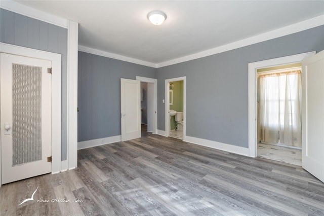 unfurnished bedroom with baseboards, ensuite bath, ornamental molding, and wood finished floors
