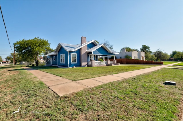 view of front facade featuring a chimney, a front yard, fence, and metal roof