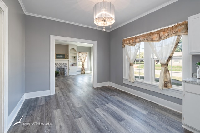 empty room featuring crown molding, a tiled fireplace, dark wood-type flooring, and a chandelier