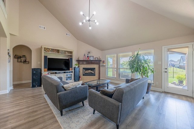 living room featuring an inviting chandelier, light hardwood / wood-style flooring, high vaulted ceiling, and a tile fireplace