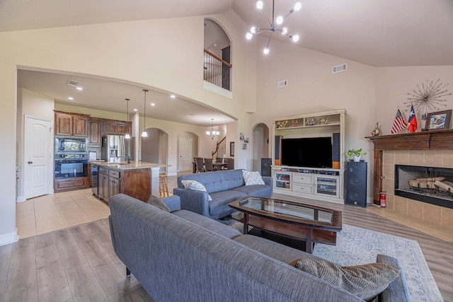 living room featuring light wood-type flooring, a tiled fireplace, a chandelier, and high vaulted ceiling