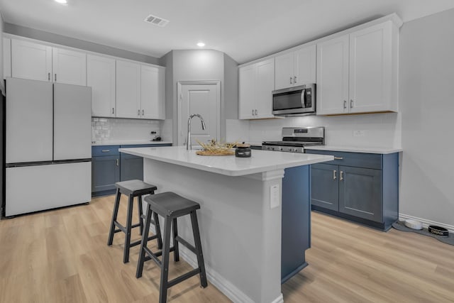 kitchen with light wood-type flooring, a kitchen island with sink, white cabinets, a kitchen bar, and appliances with stainless steel finishes