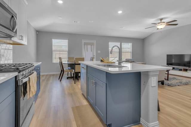 kitchen featuring appliances with stainless steel finishes, white cabinets, light wood-type flooring, a kitchen island with sink, and sink