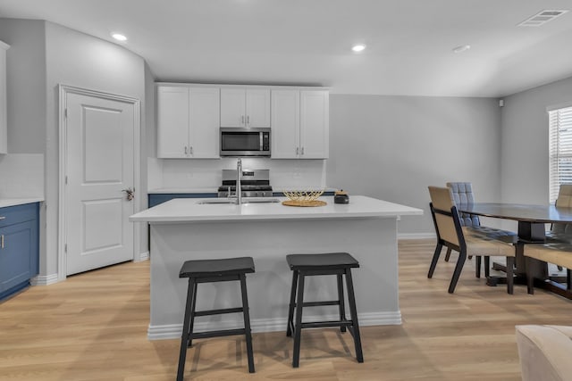 kitchen featuring appliances with stainless steel finishes, white cabinets, light wood-type flooring, a center island with sink, and sink