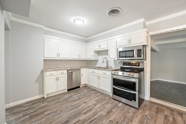 kitchen with appliances with stainless steel finishes, tasteful backsplash, white cabinets, hardwood / wood-style floors, and sink