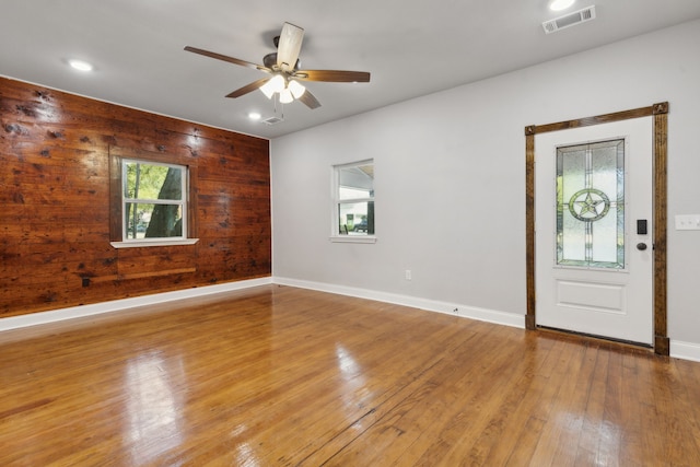 unfurnished room with wood walls, light hardwood / wood-style flooring, and ceiling fan