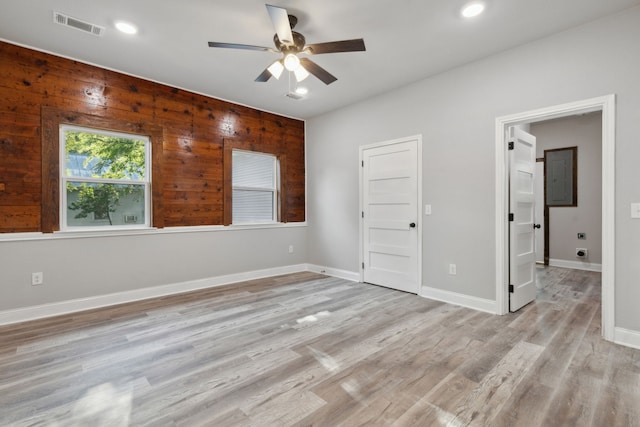 unfurnished bedroom featuring ceiling fan, wood walls, and light hardwood / wood-style flooring