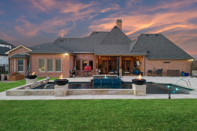 back house at dusk featuring a lawn, a swimming pool with hot tub, pool water feature, and a patio area