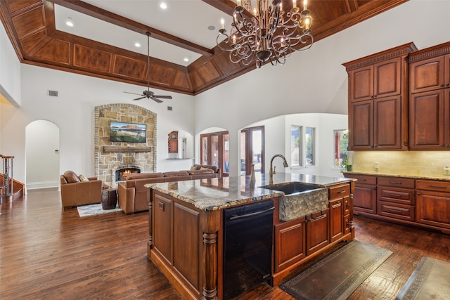 kitchen featuring an island with sink, ceiling fan with notable chandelier, a fireplace, and high vaulted ceiling