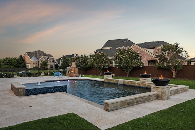 pool at dusk with a patio, a lawn, and pool water feature