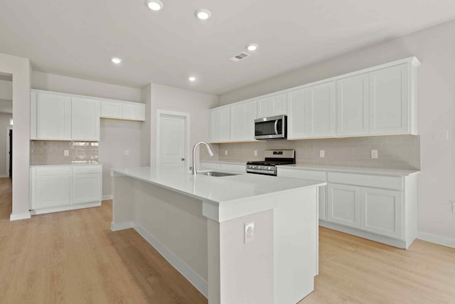 kitchen with appliances with stainless steel finishes, sink, a center island with sink, and white cabinets