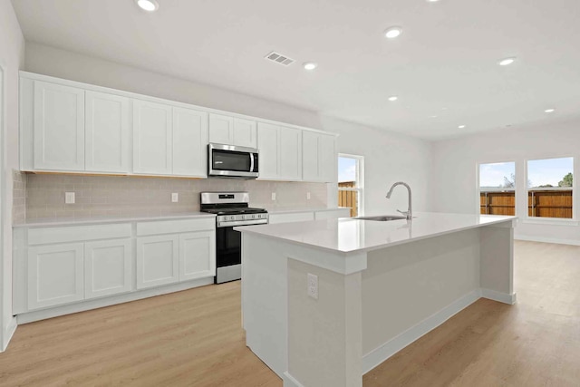 kitchen featuring appliances with stainless steel finishes, white cabinetry, an island with sink, sink, and light wood-type flooring