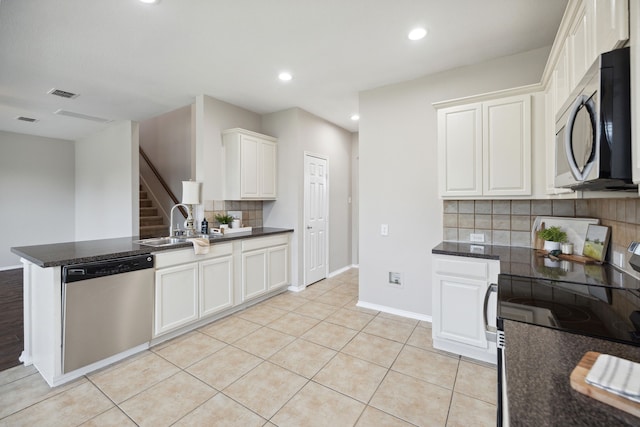 kitchen with tasteful backsplash, white cabinets, light tile patterned floors, and appliances with stainless steel finishes