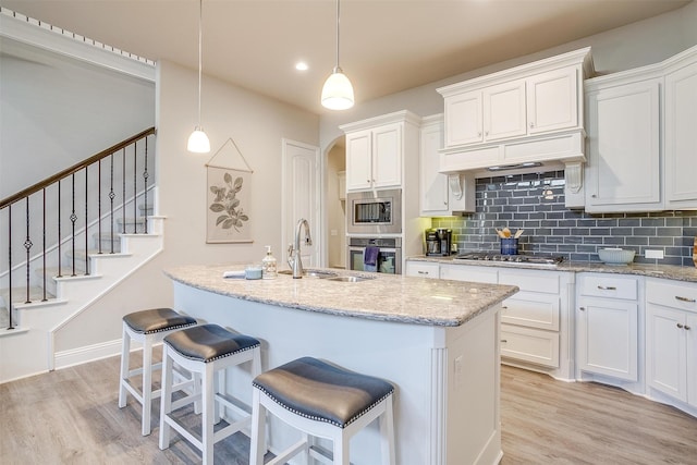 kitchen featuring appliances with stainless steel finishes, white cabinetry, light wood-type flooring, decorative light fixtures, and sink