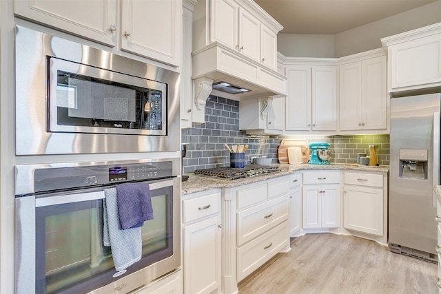 kitchen with white cabinets, appliances with stainless steel finishes, light stone countertops, light hardwood / wood-style floors, and decorative backsplash