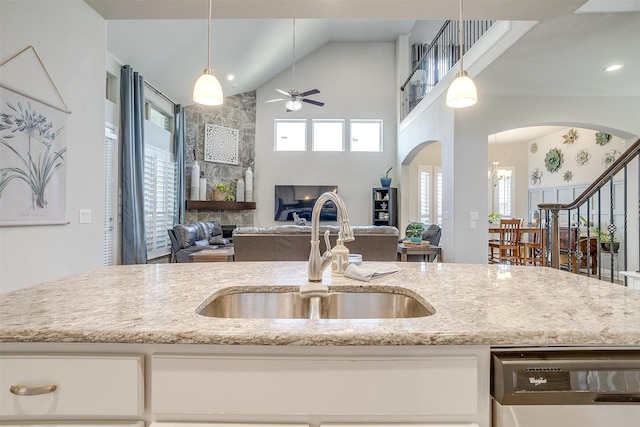 kitchen with ceiling fan, a stone fireplace, light stone countertops, and sink