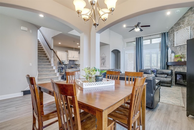 dining area with ceiling fan with notable chandelier, a fireplace, and light wood-type flooring