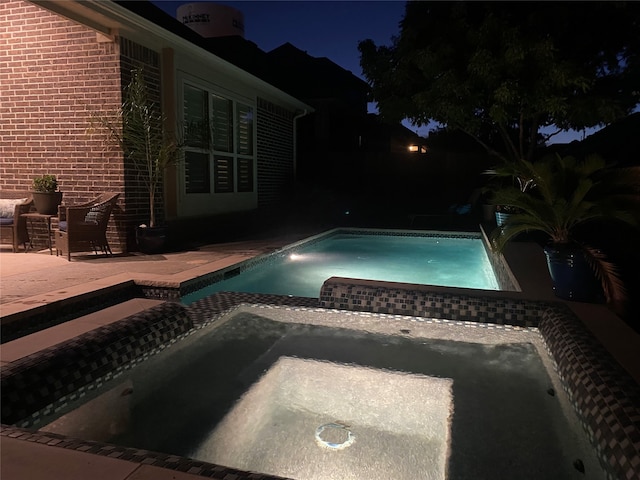 pool at twilight with an in ground hot tub and a patio area