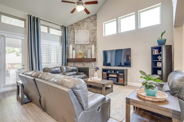 living room featuring ceiling fan, light hardwood / wood-style flooring, high vaulted ceiling, and a large fireplace