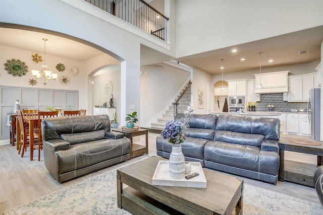 living room featuring a notable chandelier, light hardwood / wood-style flooring, and a towering ceiling