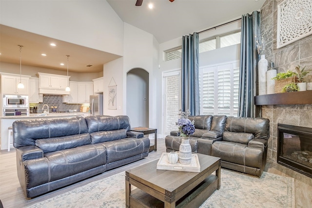 living room featuring ceiling fan, sink, a stone fireplace, light hardwood / wood-style flooring, and a towering ceiling