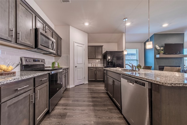 kitchen with pendant lighting, an island with sink, backsplash, stainless steel appliances, and dark hardwood / wood-style flooring