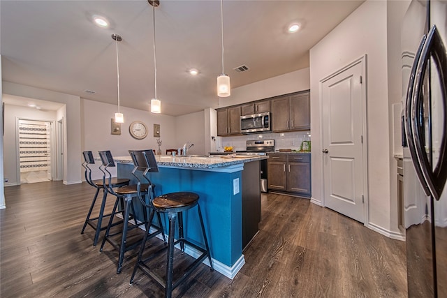 kitchen featuring dark wood-type flooring, an island with sink, a kitchen breakfast bar, stainless steel appliances, and decorative light fixtures