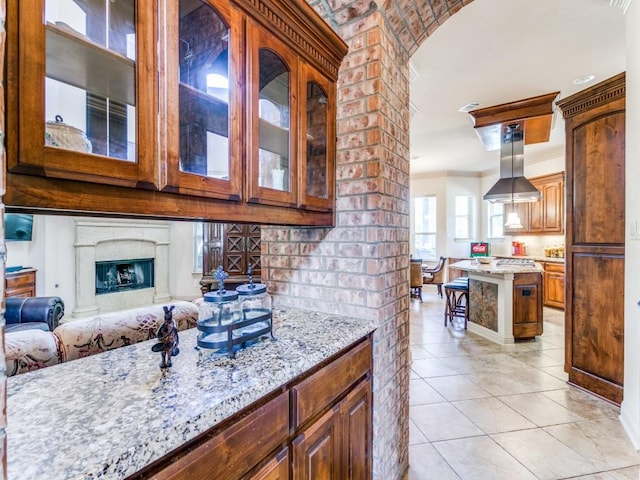 kitchen featuring light stone countertops, hanging light fixtures, crown molding, island range hood, and a fireplace