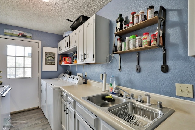 laundry area with sink, a textured ceiling, light hardwood / wood-style flooring, cabinets, and washer and dryer