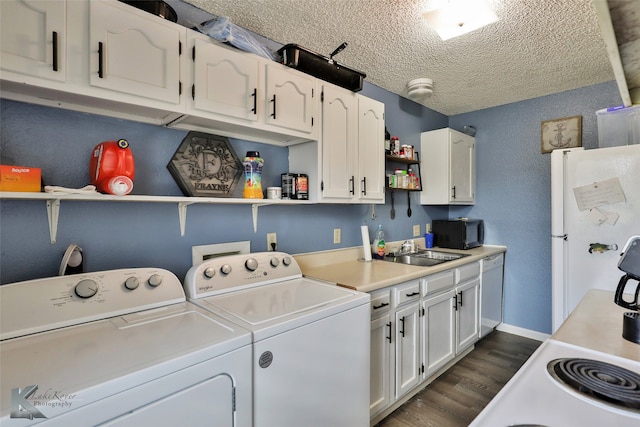 clothes washing area featuring washer and clothes dryer, a textured ceiling, sink, and dark hardwood / wood-style flooring