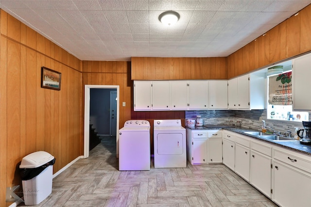 clothes washing area featuring light parquet flooring, wood walls, sink, and independent washer and dryer