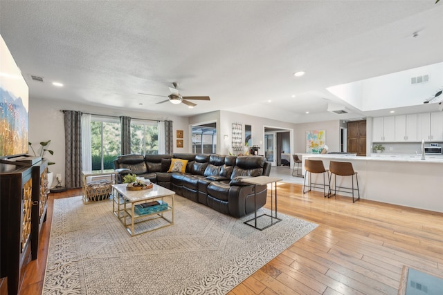 living room with sink, a skylight, light hardwood / wood-style flooring, ceiling fan, and a textured ceiling