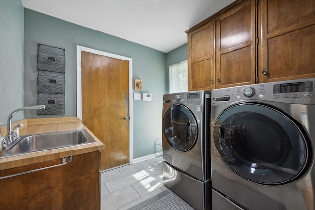 clothes washing area featuring washer and dryer, sink, light tile patterned floors, and cabinets