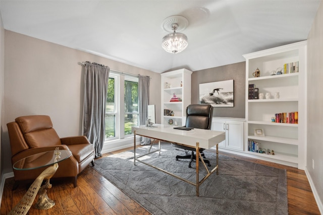 office space featuring dark hardwood / wood-style floors, built in features, lofted ceiling, and an inviting chandelier